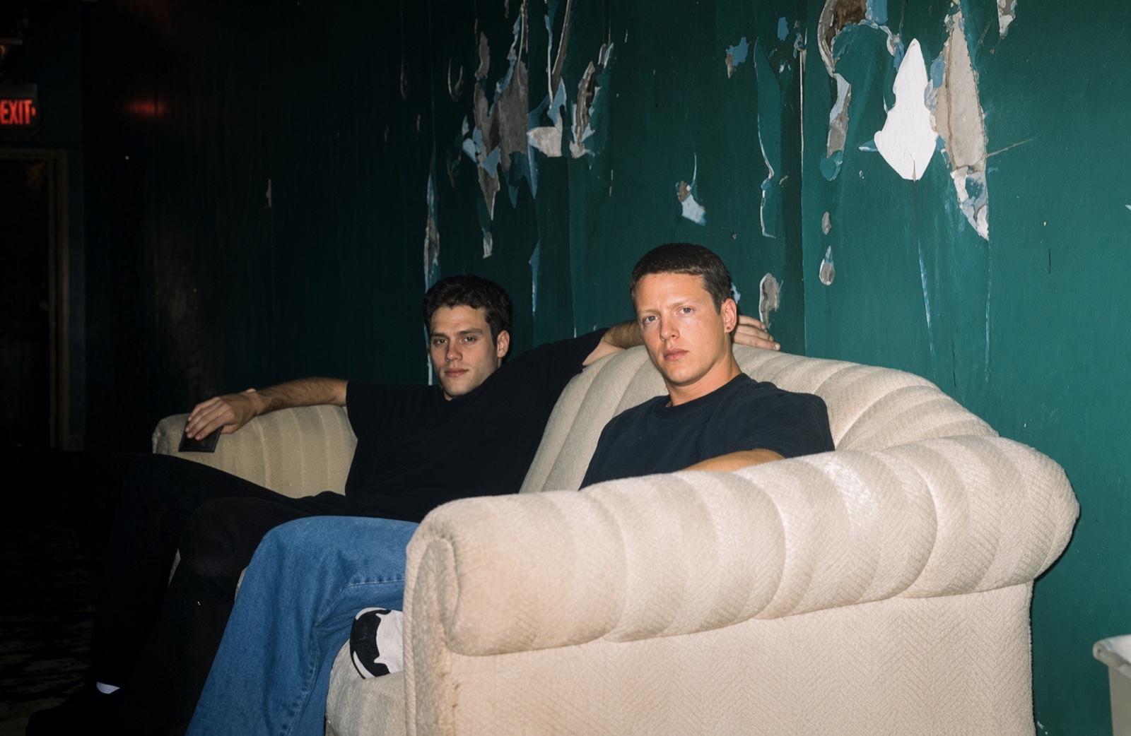 Two people seated on a cream sofa against a weathered teal wall